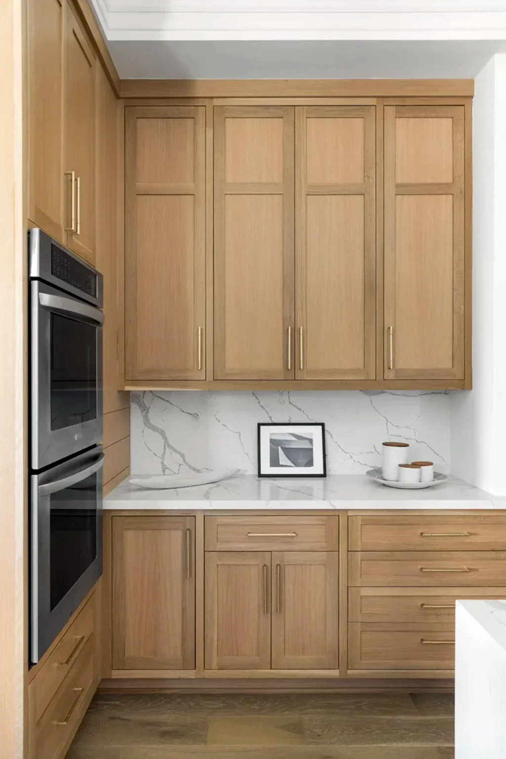 Tall oak cabinetry flanking a wall oven with a marble backsplash