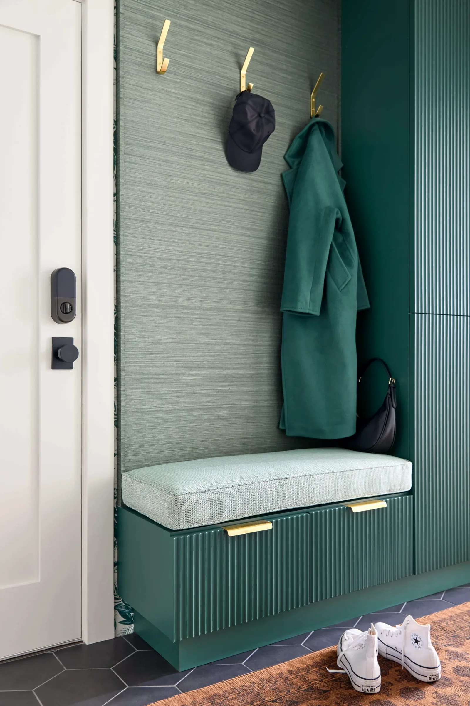 Mudroom with brass hooks, coats hung above the fluted bench