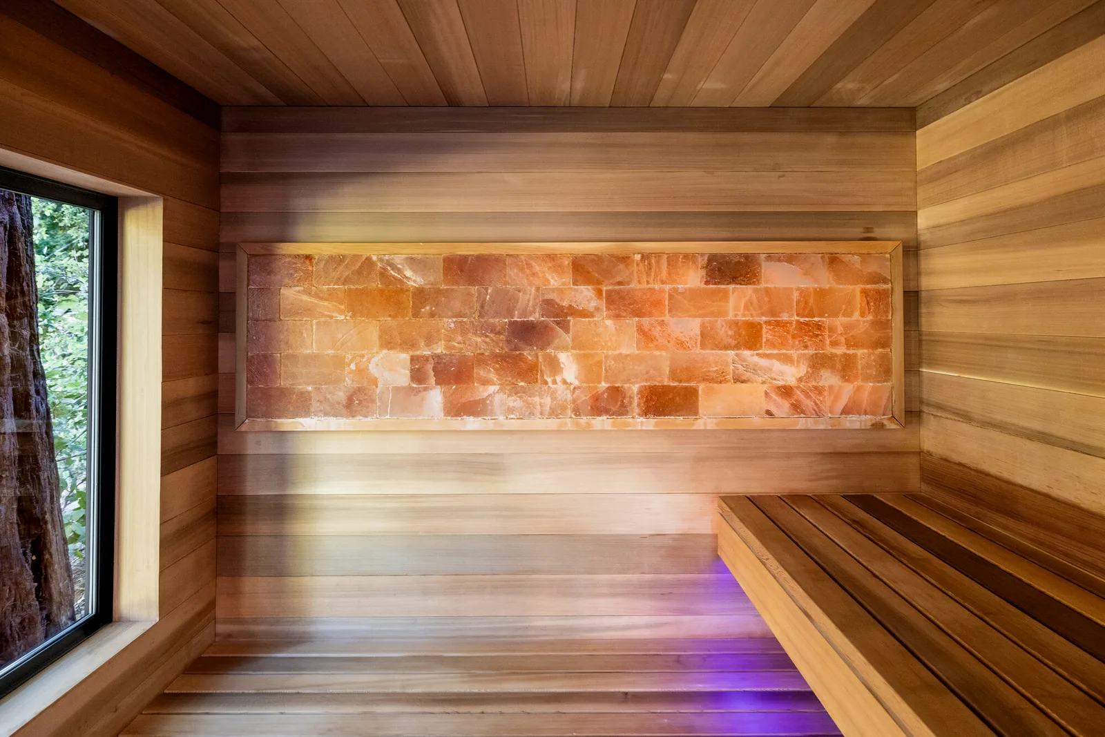 Sauna interior with a lit salt panel and a window onto the garden